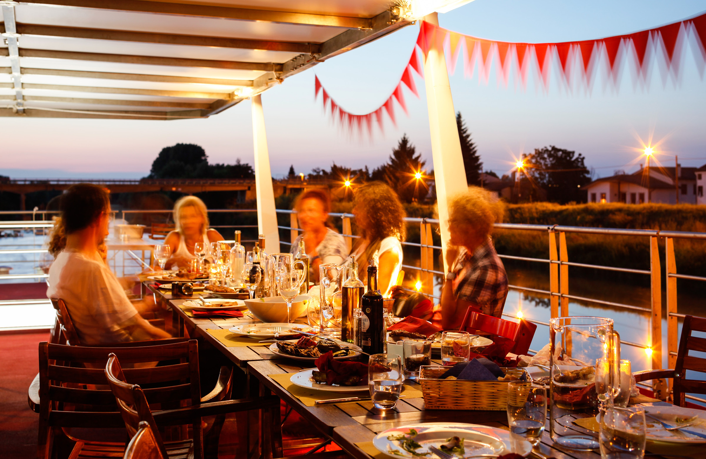 People chatting in front of a set table on the sun deck of the barge Ave Maria, Girolibero