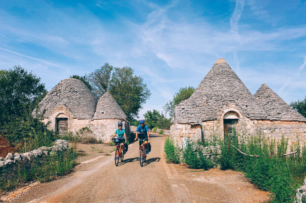 Cyclists riding past trulli houses, Alberobello, Puglia cycling tour