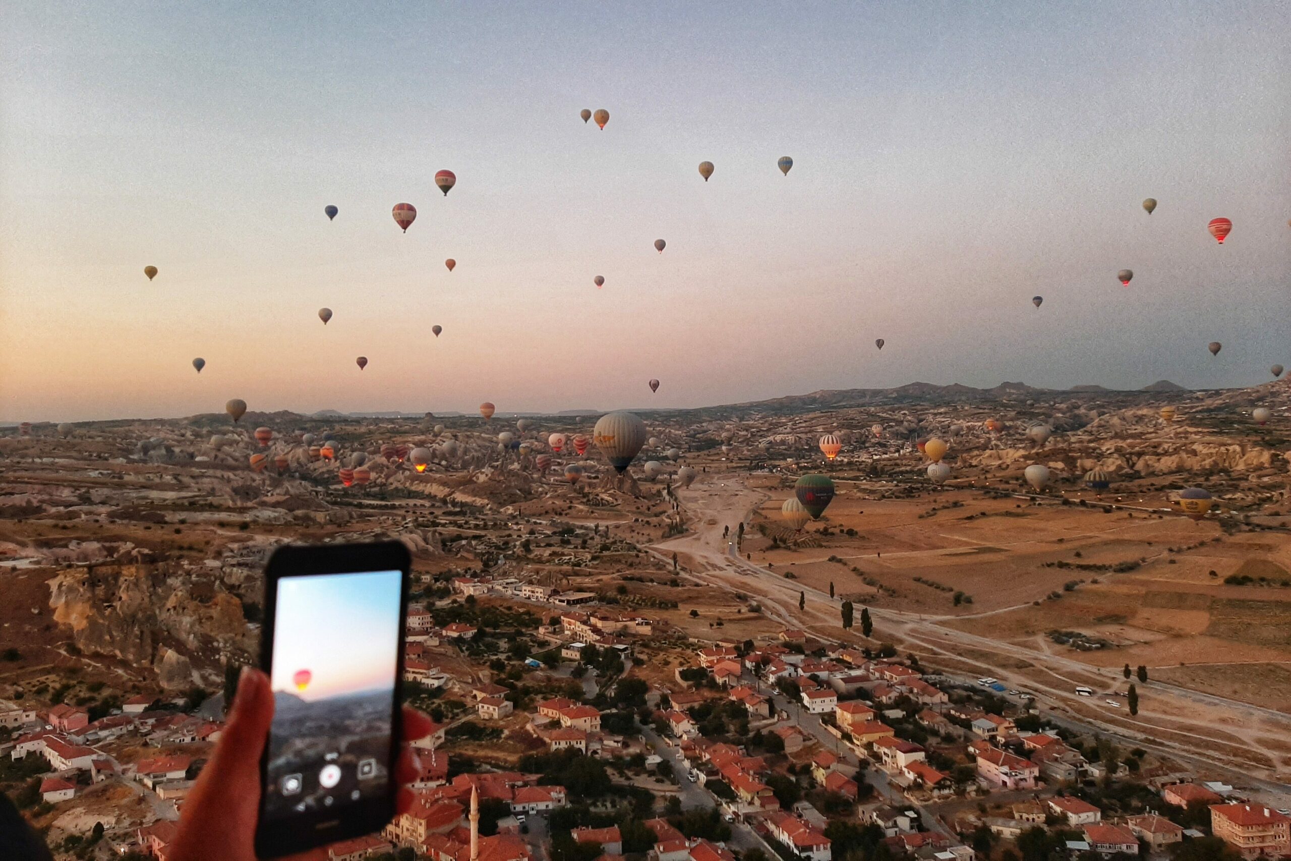 Sunrise in Cappadocia, Turkey: dozens of colorful hot air balloons fly over Göreme Valley and fairy chimneys, filmed by a tourist with smartphone