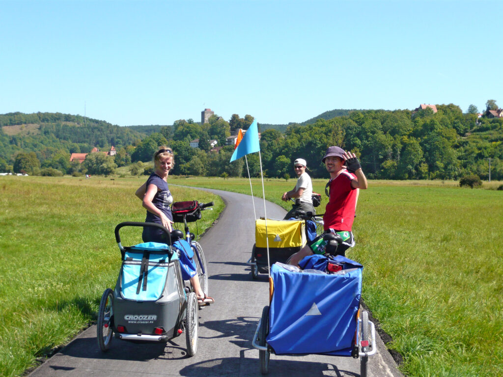 Family cycling with children's trailers along a green countryside path