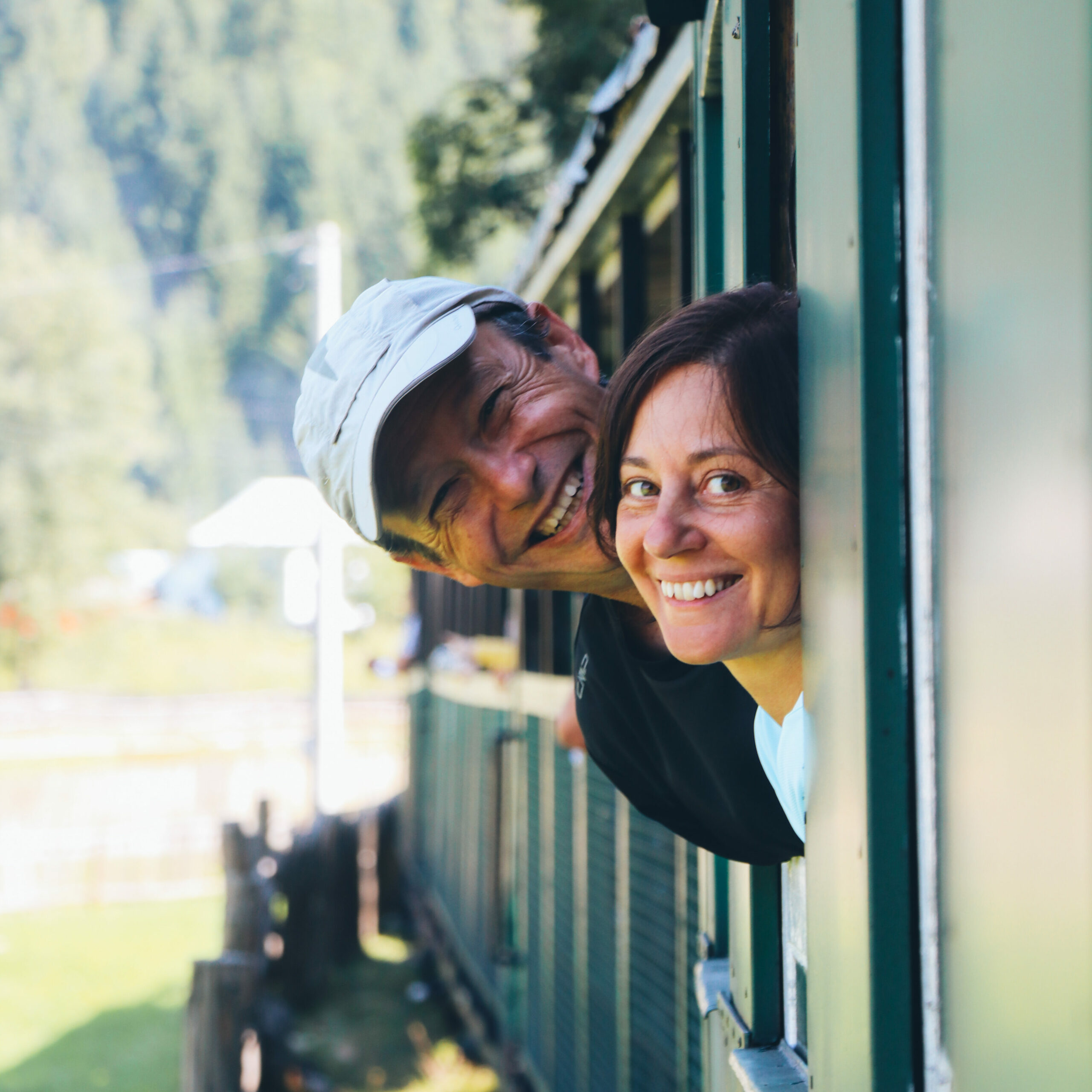 Couple smiling out of a vintage train window during a cycling holiday